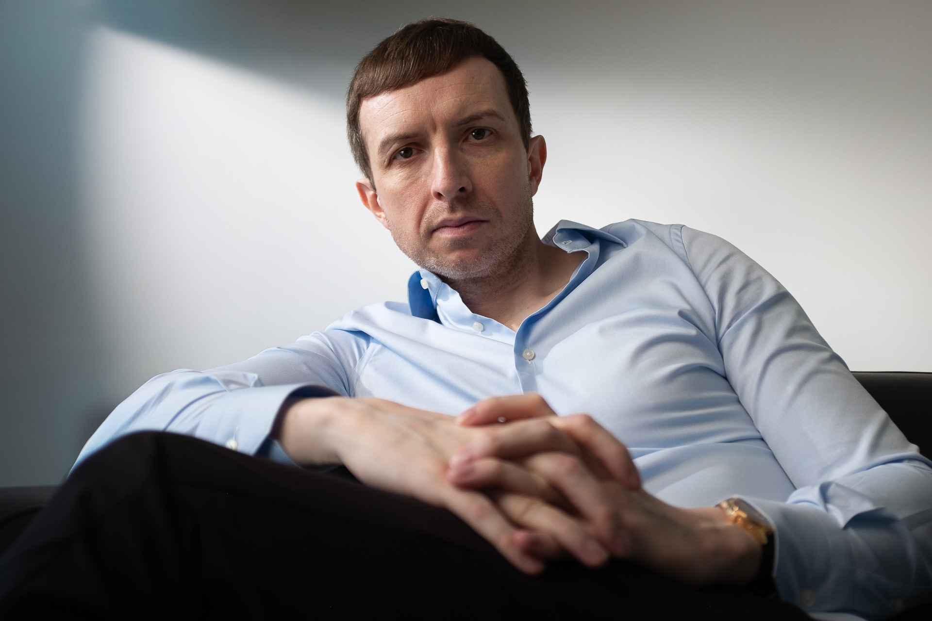 Michael Serwa - the best life coach in Europe, wearing a light blue shirt and sitting on a sofa in his apartment in South Kensignton